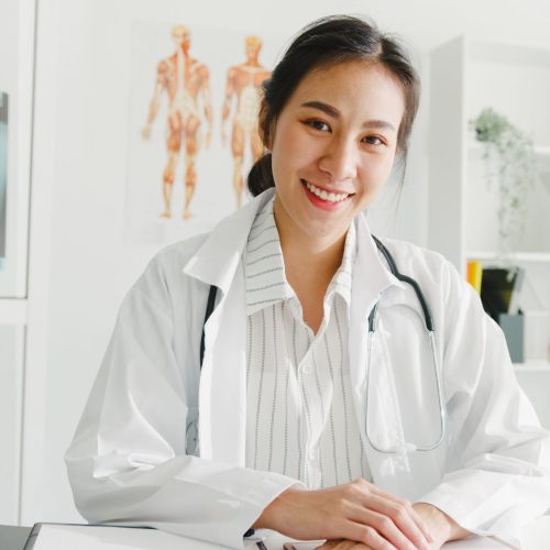 Confident young Asia female doctor in white medical uniform with stethoscope looking at camera and smiling while video conference call with patient in health hospital. Consulting and therapy concept.